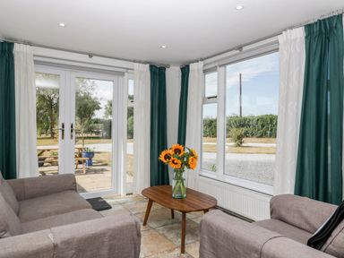 A sitting area with two armchairs a wooden coffee table with a vase of sunflowers and large windows with green and white curtains at Somerset House in Othery near Middlezoy