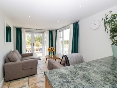 A living room with two sofas a wooden coffee table with sunflowers and green curtains at Somerset House in Othery near Middlezoy