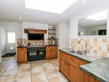 A kitchen with wooden cabinets a black stove and oven a double sink with a green countertop and a mirror on the wall at Somerset House in Othery near Middlezoy