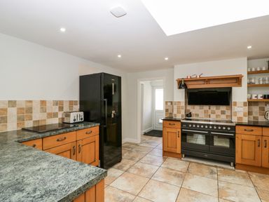 A kitchen with wooden cabinets black refrigerator black oven tiled floor and tiled backsplash at Somerset House in Othery near Middlezoy