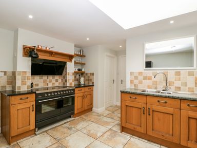 A kitchen with wooden cabinets, a black stove and oven, a double sink, tiled backsplash, and tiled floor at Somerset House in Othery near Middlezoy