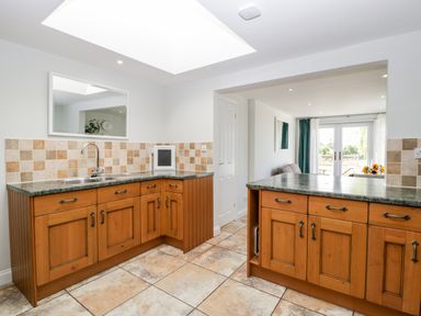 A kitchen with wooden cabinets tiled floor and a window opening to a living area at Somerset House in Othery near Middlezoy