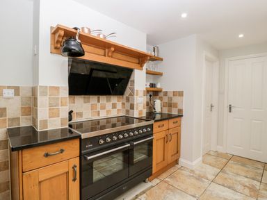 A kitchen with a black stove and oven surrounded by wooden cabinets and tiled walls at Somerset House in Othery near Middlezoy
