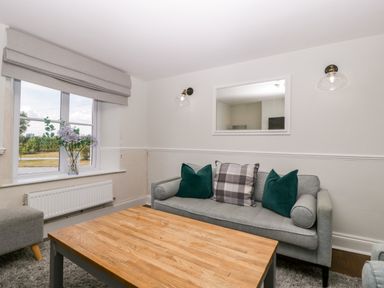 A living room with a gray sofa and a wooden coffee table by a window with flowers at Somerset House Othery near Middlezoy