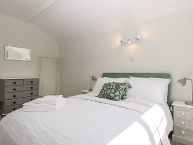 A bedroom with a bed a green headboard two bedside tables with lamps a grey chest of drawers and a mirror at Somerset House in Othery near Middlezoy