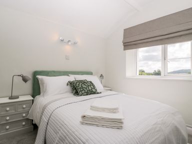 A bedroom with a bed with white bedding and green cushions two bedside tables with lamps and a window with beige blinds at Somerset House in Othery near Middlezoy