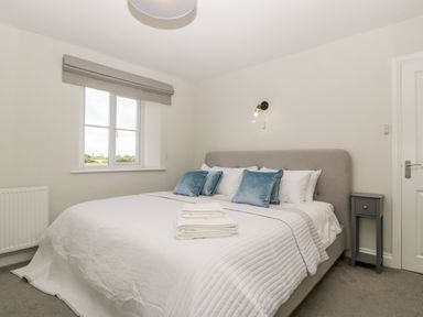 A bedroom with a large bed with pillows and folded towels near a window and a small bedside table at Somerset House in Othery near Middlezoy