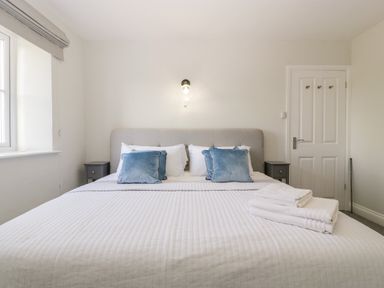 A bedroom with a large bed blue pillows folded towels on bed bedside tables and a window at Somerset House in Othery near Middlezoy
