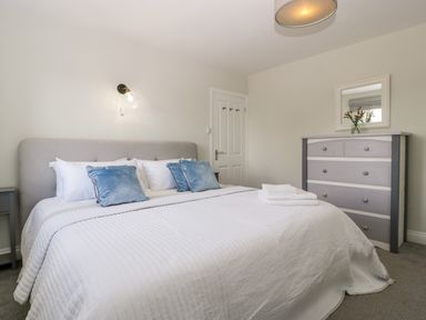 A bedroom with a double bed with blue cushions a dresser with a mirror and flowers at Somerset House in Othery near Middlezoy