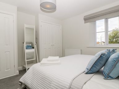 A bedroom with a bed with blue pillows and white towels on it a standing mirror two closed doors and a window at Somerset House in Othery near Middlezoy