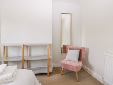 A small pink chair with two cushions next to a tall mirror and a simple shelf in a bedroom at Somerset House in Othery near Middlezoy