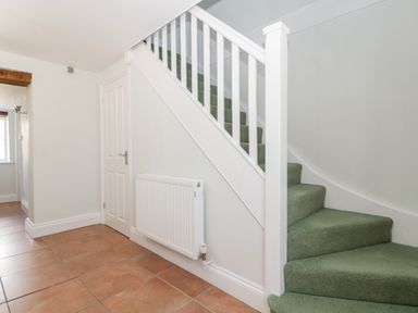 A staircase with green carpet and white railing next to a door and radiator on tiled floor at Somerset House in Othery near Middlezoy