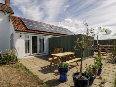 A patio area with a wooden picnic table bench and potted plants outside a white house with solar panels on the roof at Somerset House in Othery near Middlezoy