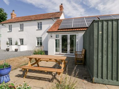 A white house with solar panels on the roof a wooden picnic table and bench on a patio at Somerset House in Othery near Middlezoy