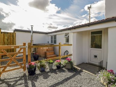 An outdoor area with a wooden gate, a hot tub with steps, gravel ground, potted plants, and a white door with a pet flap at Somerset House in Othery near Middlezoy