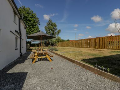 A backyard with a wooden picnic table and umbrella near a white house and a wooden fence at Somerset House in Othery near Middlezoy