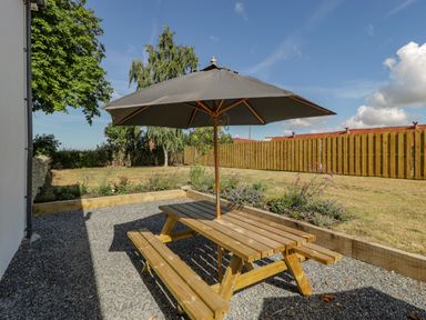 A wooden picnic table with an umbrella on a gravel patio next to a garden with grass and flowers at Somerset House in Othery near Middlezoy