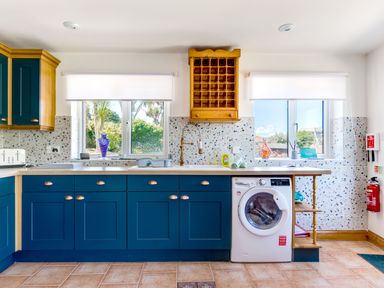 A kitchen with blue cabinets a washing machine and two windows at Baywatch Sands in Polzeath