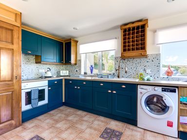 A kitchen with blue cabinets white appliances and windows with white blinds at Baywatch Sands Polzeath