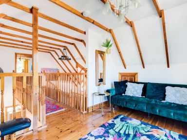 A sitting area with a green sofa pillows a small round table wooden beams on the ceiling and a floral rug at Baywatch Sands Polzeath
