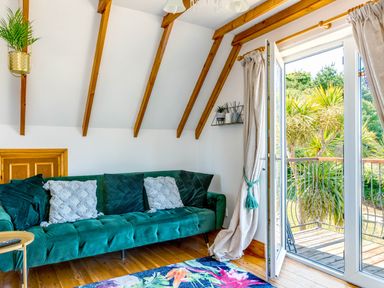 A sitting room with a green sofa cushions a rug and open doors leading to a balcony at Baywatch Sands Polzeath