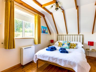 A bedroom with a bed with white bedding and blue towels on it yellow curtains and wooden ceiling beams at Baywatch Sands in Polzeath