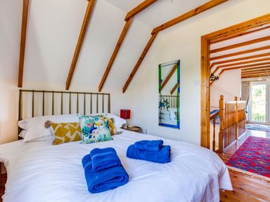 A bedroom with a bed with colorful pillows and folded blue towels with wooden beams on the ceiling at Baywatch Sands in Polzeath