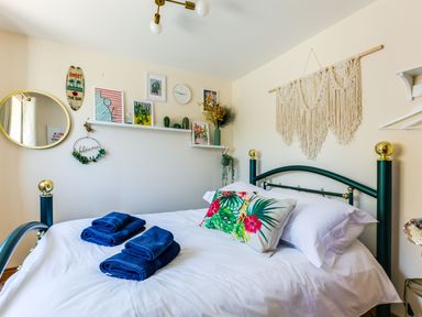 A bedroom with a bed with white sheets and blue towels on it and wall art above the bed at Baywatch Sands Polzeath