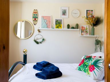 A bedroom with a bed with floral pillows and folded blue towels with wall art and decorations at Baywatch Sands in Polzeath