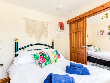 A bedroom with a bed with floral pillows blue towels and a wooden sliding door at Baywatch Sands in Polzeath