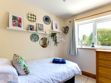 A bedroom with a single bed a pillow and blue towel on the bed decorative shelves and window with curtains at Baywatch Sands in Polzeath