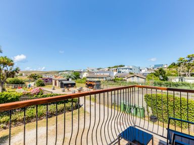 View from a balcony with metal railing overlooking houses green bins and a yard with tables at Baywatch Sands in Polzeath