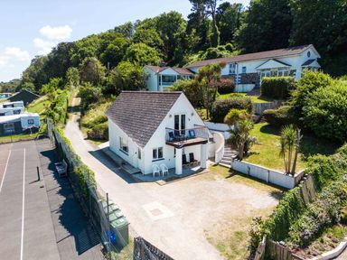 A property with two white houses surrounded by greenery with a tennis court next to it at Baywatch Sands in Polzeath