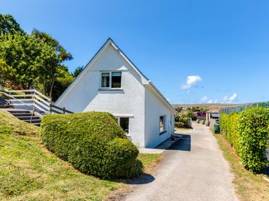A white triangular house with bushes and a driveway at Baywatch Sands in Polzeath