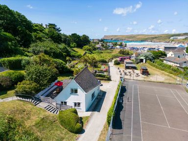 A house near a paved sports court with seating and a view of the beach at Baywatch Sands in Polzeath
