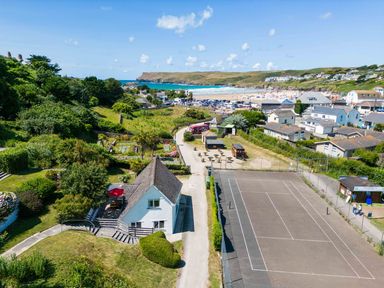 A coastal area with a tennis court a white house green hills and a beach in the background at Baywatch Sands Polzeath
