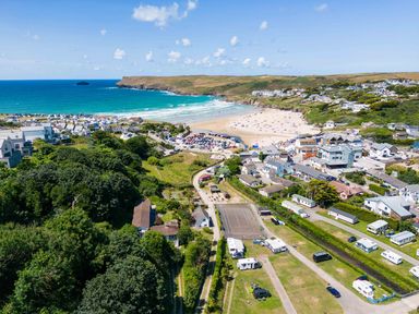 An aerial view of a coastal town with a beach parking area houses caravans and a sports court at Baywatch Sands in Polzeath