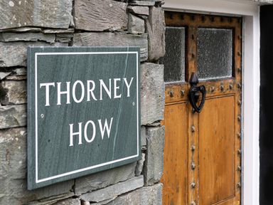 A stone wall with a green sign reading Thorney How next to a wooden door with glass panels