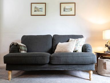 A dark gray sofa with two pillows and a blanket next to a wooden side table with a lamp at Thorney How in Grasmere