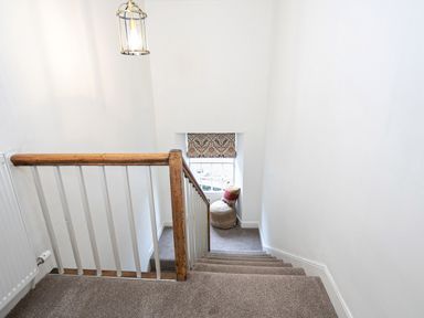 A staircase with carpeted steps wooden banister and a small window with patterned blind and a cushion seat at Thorney How in Grasmere