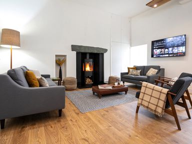 A living room with grey sofas and armchairs wooden floor and a wall mounted tv at Thorney How in Grasmere