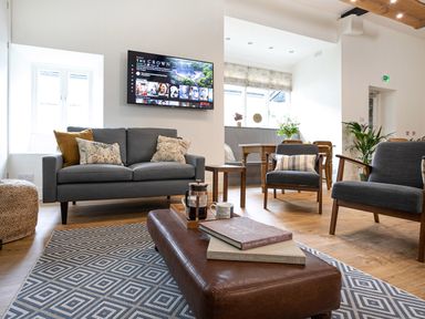 A living room with a grey sofa cushions armchairs a wooden coffee table and a wall-mounted television at Thorney How in Grasmere