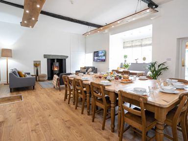 A dining area with a wooden table set with bowls and glasses next to a living space with sofas and a fireplace at Thorney How in Grasmere