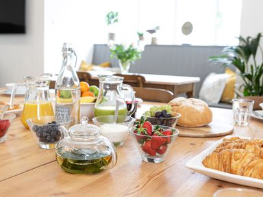 A wooden table with bowls of fruit including strawberries and grapes a glass teapot with tea croissants and bread at Thorney How in Grasmere