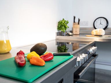 A kitchen counter with colorful peppers and an avocado on a cutting board and a loaf of bread near a clock at Thorney How in Grasmere