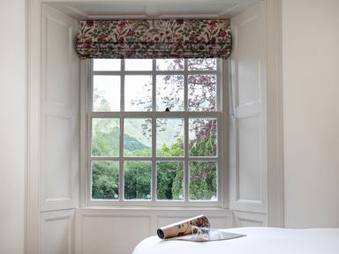 A window with a floral Roman blind and a view of trees and hills at Thorney How in Grasmere