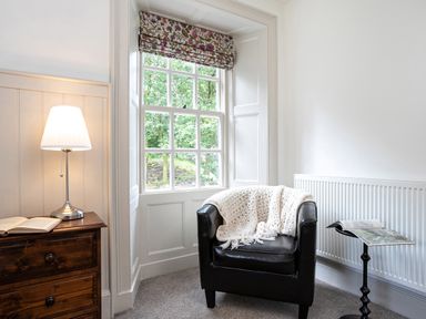 A black armchair with a white blanket next to a window and wooden chest with lamp at Thorney How in Grasmere