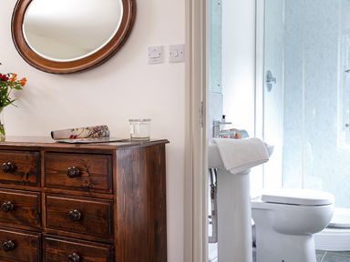 A wooden dresser with a round mirror above it and a bathroom with a white sink and toilet at Thorney How in Grasmere