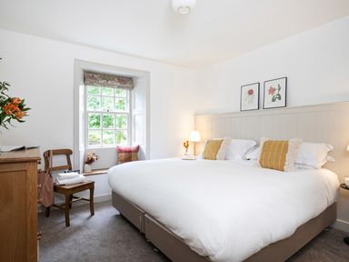 A bedroom with a large bed two yellow pillows a wooden chair with towels a chest of drawers and a window with a seat at Thorney How in Grasmere