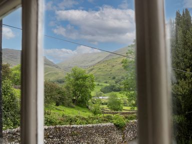 A view of green hills and trees through a window at Thorney How in Grasmere
